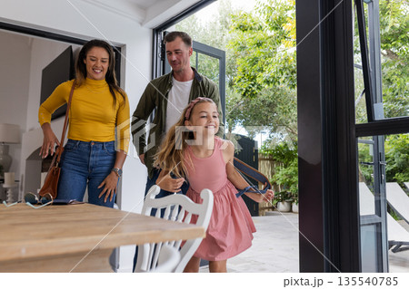 Happy family entering home, young girl joyfully leading parents through doorway 135540785