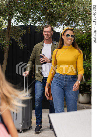 Couple arriving at home with suitcase, smiling and enjoying sunny day Couple arriving at home with suitcase, smiling and enjoying sunny day 135540802