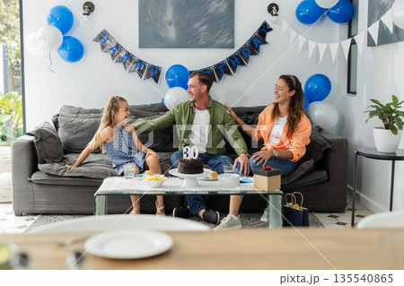 Celebrating birthday, happy family sitting on couch with cake and decorations Celebrating birthday, happy family sitting on couch with cake and decorations 135540865