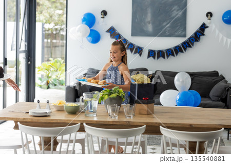 Young girl setting table with snacks for birthday party at home, smiling happily Young girl setting table with snacks for birthday party at home, smiling happily 135540881