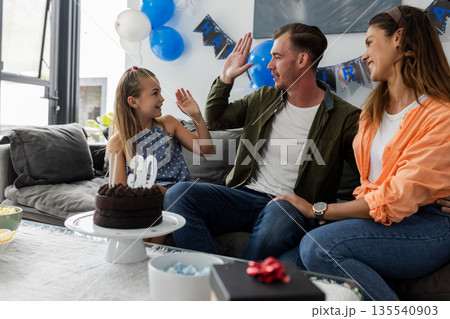 Celebrating birthday, family giving high fives on couch with cake and balloons Celebrating birthday, family giving high fives on couch with cake and balloons 135540903