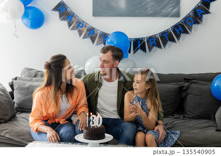 Family sitting on couch with cake and balloons, celebrating birthday together 135540905