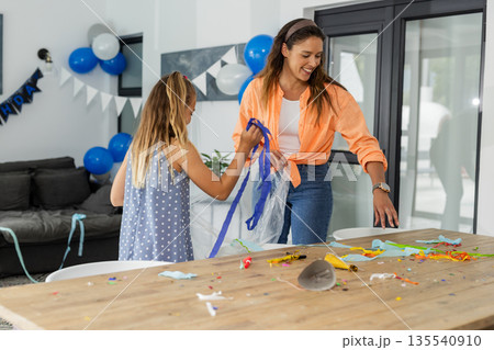 Mother and daughter cleaning up after birthday party at home, smiling together 135540910