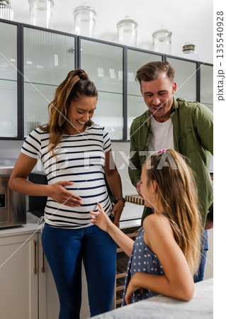Expectant parents smiling as daughter touches mother's pregnant belly in kitchen Expectant parents smiling as daughter touches mother's pregnant belly in kitchen 135540928