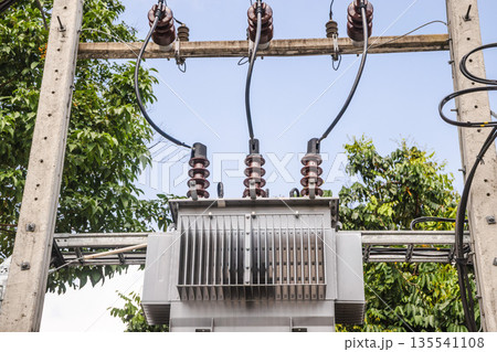 Electrical transformer and power lines on utility pole in tropical Thailand landscape, energy infrastructure surrounded by green trees and clear sky 135541108