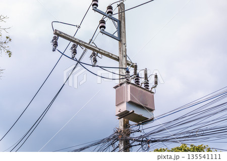 Electrical transformer and power lines on utility pole against cloudy sky, urban energy infrastructure scene 135541111