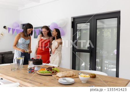 Laughing and chatting, three young women gather around chocolate cake at home Laughing and chatting, three young women gather around chocolate cake at home 135541423