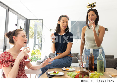 Celebrating indoors, three young women with diverse backgrounds enjoy casual gathering with wine 135541475