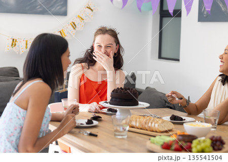 Laughing and enjoying cake, three young women gather at birthday celebration 135541504