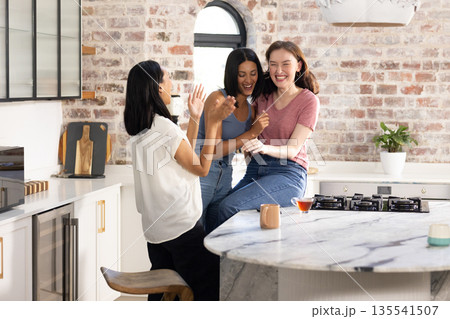 Laughing together in modern kitchen, three young women enjoy joyful moment Laughing together in modern kitchen, three young women enjoy joyful moment 135541507