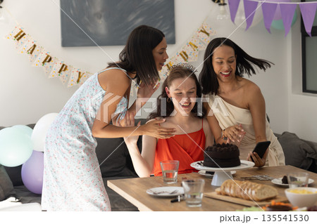 Celebrating birthday, three young women gather around chocolate cake at home Celebrating birthday, three young women gather around chocolate cake at home 135541530