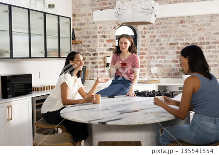 Laughing and chatting, three women gather around marble kitchen island Laughing and chatting, three women gather around marble kitchen island 135541554