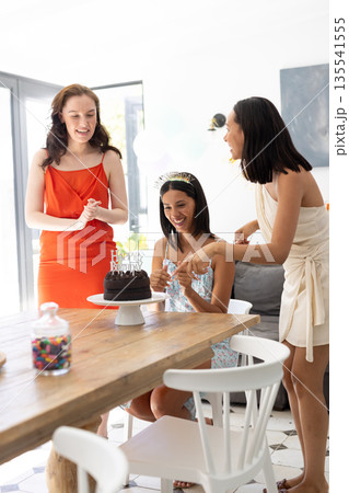 Laughing and celebrating, three young women gather around birthday cake at home Laughing and celebrating, three young women gather around birthday cake at home 135541555