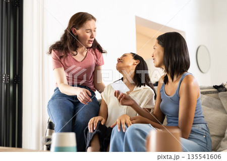 Laughing together on cozy sofa, three young women share joyful moment 135541606