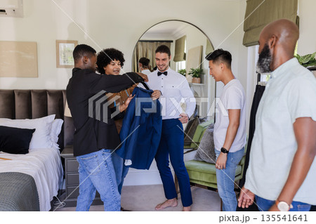Groom and friends preparing for wedding, sharing laughter and adjusting suit jacket 135541641