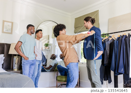 Friends helping groom try on suit in bedroom, preparing for wedding day Friends helping groom try on suit in bedroom, preparing for wedding day 135541645