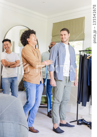 Friends laughing while measuring groom for wedding suit in cozy room 135541678