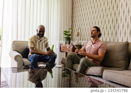 Two men sitting on sofa enjoying drinks in cozy living room setting Two men sitting on sofa enjoying drinks in cozy living room setting 135541798