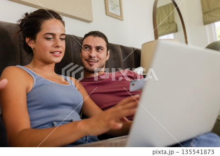 Couple shopping online using laptop, smiling and enjoying time together at home 135541873