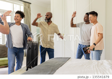 Friends celebrating with high fives in bedroom, holding suitcase and smartphone Friends celebrating with high fives in bedroom, holding suitcase and smartphone 135541879