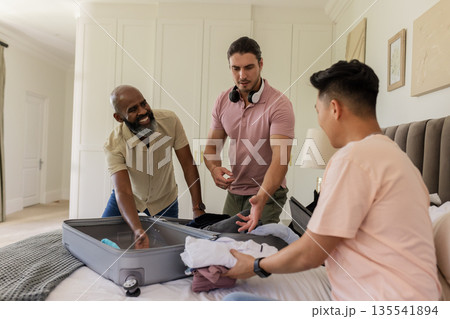 Friends packing suitcase together in bedroom, preparing for wedding celebration Friends packing suitcase together in bedroom, preparing for wedding celebration 135541894