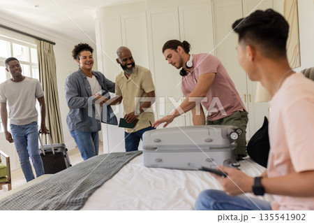 Friends gathering in bedroom, packing suitcase and sharing joyful moments together 135541902