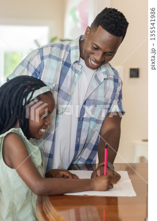 African American father helping daughter with homework at home, both smiling happily 135541986