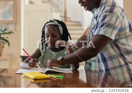 Father helping daughter with homework at home, both focused and engaged Father helping daughter with homework at home, both focused and engaged 135542016