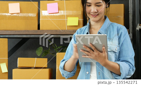 Asian woman startup small business at home office. Online seller entrepreneur young asian woman use tablet checking online order. Woman using tablet check stock goods supply delivery package shipping Asian woman startup small business at home office. Online seller entrepreneur young asian woman use tablet checking online order. Woman using tablet check stock goods supply delivery package shipping 135542271