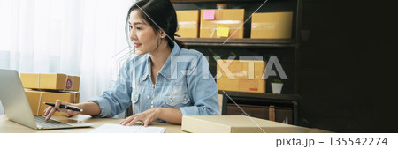 Banner Online seller Close up hands Young asian woman typing laptop keyboard checking online order on stock delivery package. Asian woman startup small business at home office with copy space 135542274