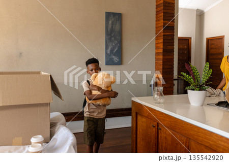 Young boy hugging teddy bear while unpacking boxes in new home 135542920
