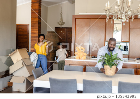 Family unpacking boxes in new home, arranging plants and organizing belongings Family unpacking boxes in new home, arranging plants and organizing belongings 135542995