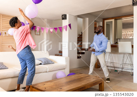 Celebrating at home, joyful couple playing with balloons in living room 135543020