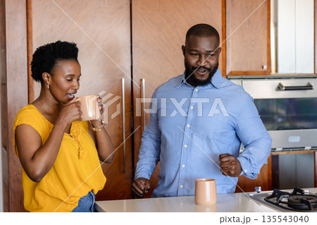 Couple enjoying morning coffee together in modern kitchen, sharing joyful moment 135543040