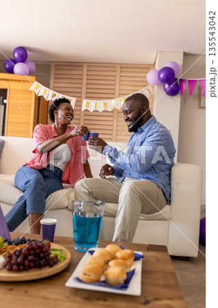Celebrating at home, joyful couple toasting with drinks on cozy sofa Celebrating at home, joyful couple toasting with drinks on cozy sofa 135543042