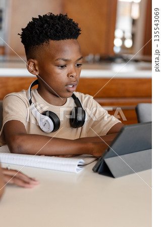 Young boy using tablet with headphones, studying at home, focused on learning 135543069