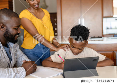 Family helping son with homework using tablet at kitchen table, smiling together 135543074