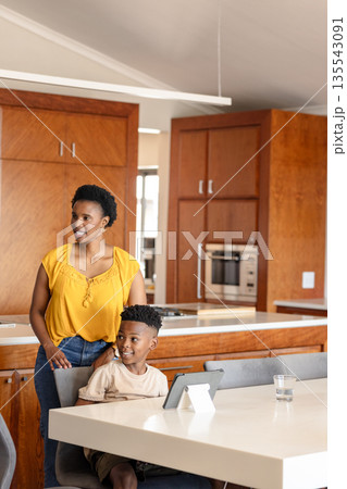 Mother and son smiling while using tablet at home in modern kitchen Mother and son smiling while using tablet at home in modern kitchen 135543091