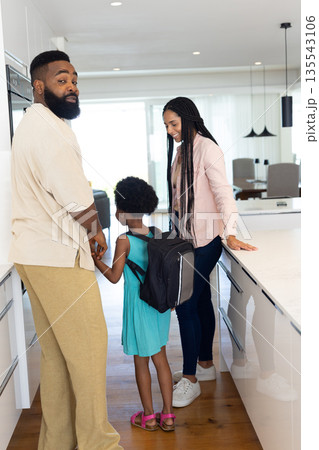 Family preparing for school, parents smiling while daughter wearing backpack 135543106