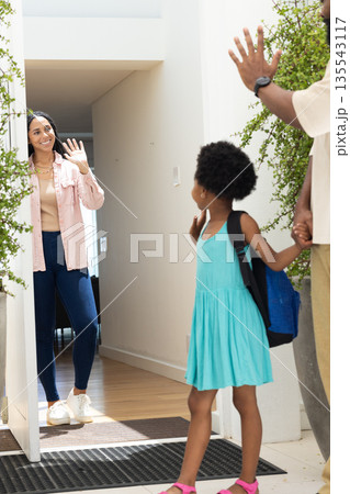 Family greeting at doorway, young girl with backpack waving and smiling warmly Family greeting at doorway, young girl with backpack waving and smiling warmly 135543117