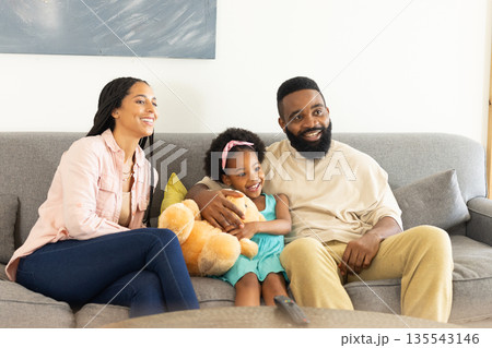 Happy family sitting on sofa, enjoying quality time with daughter and teddy bear Happy family sitting on sofa, enjoying quality time with daughter and teddy bear 135543146