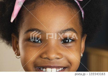 Smiling young girl with pink headband looking directly at camera, joyful expression 135543163