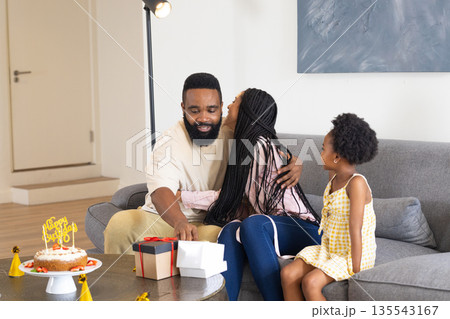 Celebrating birthday, family opening gifts and enjoying cake together in living room Celebrating birthday, family opening gifts and enjoying cake together in living room 135543167