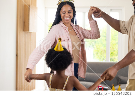 Celebrating at home, joyful family dancing together wearing party hats 135543202