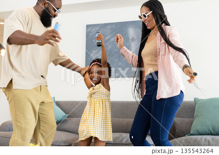 African American family dancing joyfully at home, holding microphones and smiling 135543264