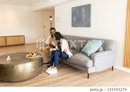 Couple sitting on sofa at home, enjoying sweet treats and sharing moment 135543274