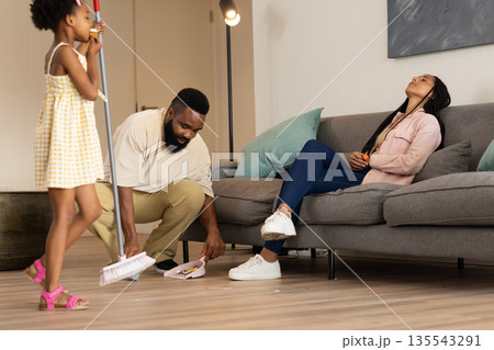 African American family cleaning living room, father sweeping while daughter helps African American family cleaning living room, father sweeping while daughter helps 135543291