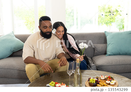 Couple relaxing on sofa, enjoying snacks and flowers in cozy living room 135543299