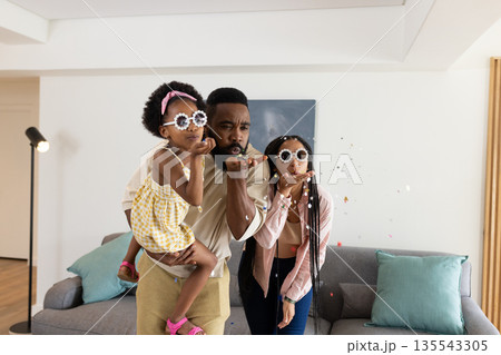 Blowing confetti in living room, African American family sharing playful moment together 135543305