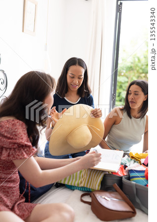Packing for vacation, three young women are in bright, cozy bedroom Packing for vacation, three young women are in bright, cozy bedroom 135543340